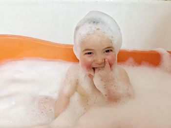 Portrait of smiling baby covered with soap sud in bathtub against wall