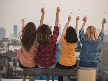 Rear view of happy friends holding illuminated sparklers while sitting in city