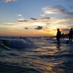 Silhouette people at beach against sky during sunset