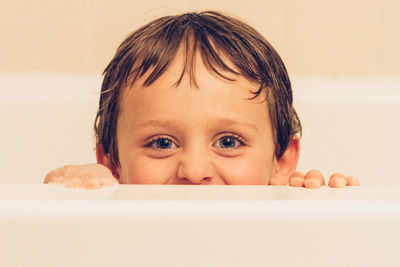 Close-up portrait of cute boy peeking by bathtub