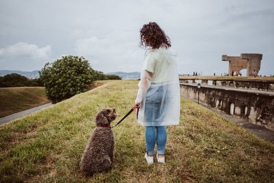 Woman with dog standing on grass against sky