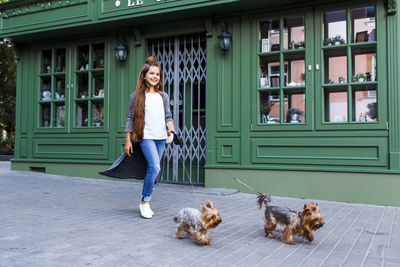 Happy girl with dogs walking on street by building in city