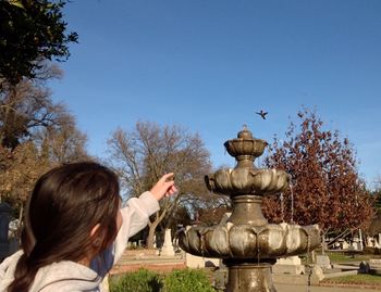 Close-up of girl pointing at bird flying against sky