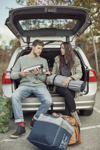 Man pouring coffee for woman while sitting at car trunk during camping