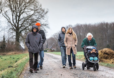 Family walking on dirt road by field against sky