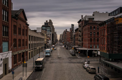 Vehicles on road amidst buildings in city against sky