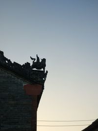 Low angle view of bird statue on roof against clear sky