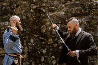 Man looking at businessman holding sword against rock formation