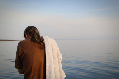 Rear view of man standing with towel by sea against sky