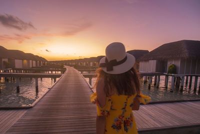 Rear view of woman standing on pier against sky during sunset