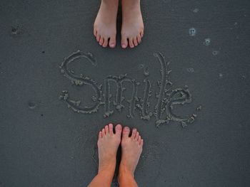Low section of couple standing by smile written on sandy beach