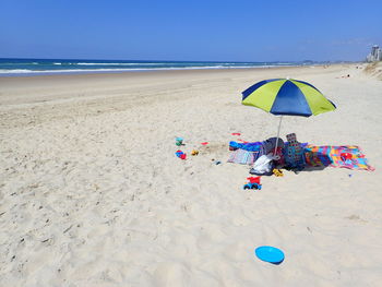 Objects under parasol at beach against clear sky