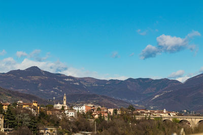 Aerial view of townscape and mountains against blue sky