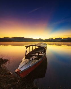 Boat moored in lake against sky during sunset