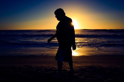 Full length of silhouette man standing on beach against sunset sky