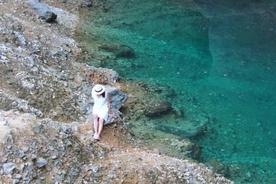 Full length of woman sitting on rock against sea