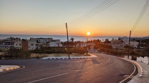 Road by city against sky during sunset