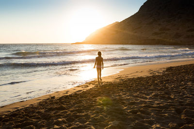 Rear view of shirtless girl walking at beach