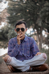 Young man wearing sunglasses smoking cigarette while sitting outdoors