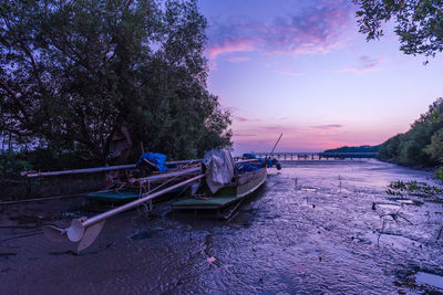 Boat moored on beach against sky during sunset