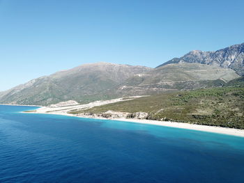 Scenic view of sea and mountains against clear blue sky