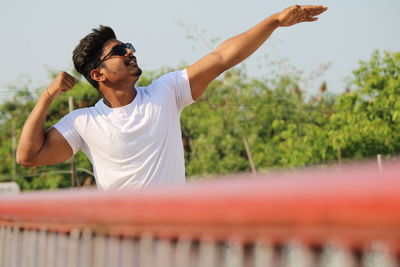 Young man standing by railing against sky