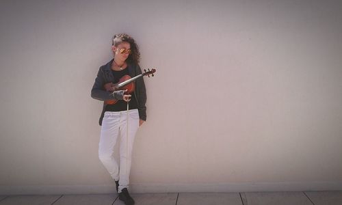 Young woman with violin standing against wall