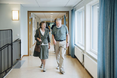 Full length of senior couple walking in alley at elderly nursing home