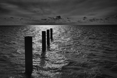 Wooden posts in sea against sky