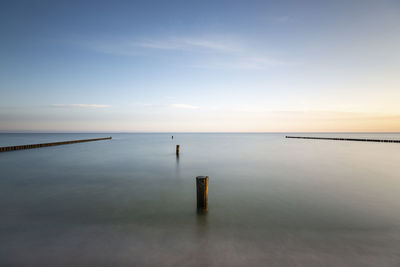 Wooden posts in sea against sky