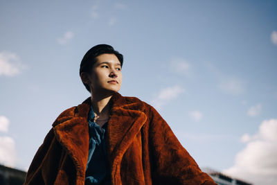 Low angle view of teenage boy looking away against sky