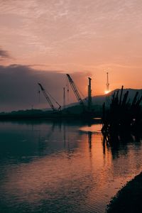 Silhouette cranes at commercial dock against sky during sunset