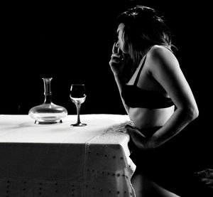 Woman with drink on table against black background