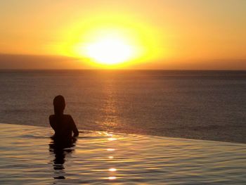 Silhouette man sitting in sea against sunset sky