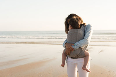 Mother carrying son while standing at beach