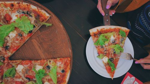 Cropped hand of woman holding pizza on table