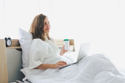 Young woman using phone while sitting on laptop