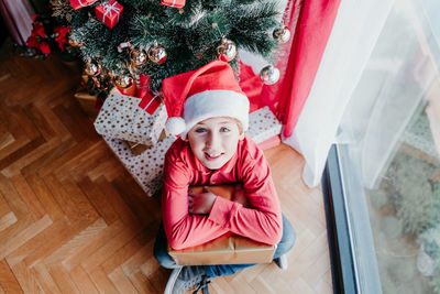 Beautiful kid boy at home with presents by the christmas tree