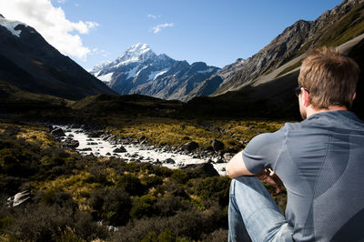 Rear view of man sitting on field against sky