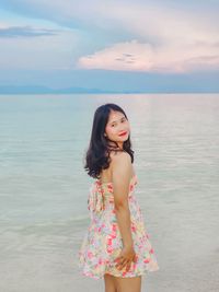 Portrait of young woman standing at beach against sky