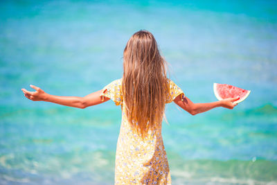 Rear view of woman with arms raised standing against sea