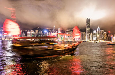 Illuminated buildings by river against sky in city at night