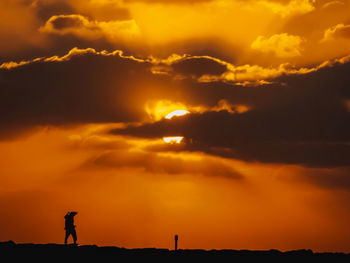 Silhouette man standing against dramatic sky during sunset