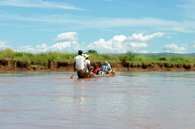 Men sitting on boat in river against sky
