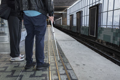 Man with white cane standing at train station