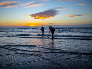 Silhouette people on beach against sky during sunset