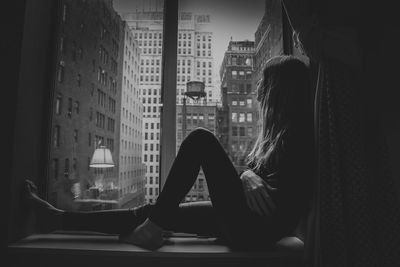 Side view of teenage girl sitting on window sill