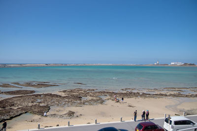 People on beach against clear blue sky