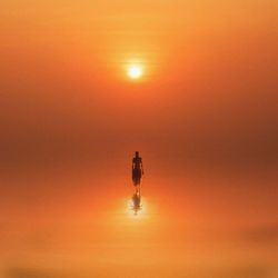 Silhouette people standing by sea against orange sky during sunset