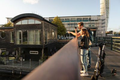 Surface level of couple photographing standing on bridge with electric push scooters in city